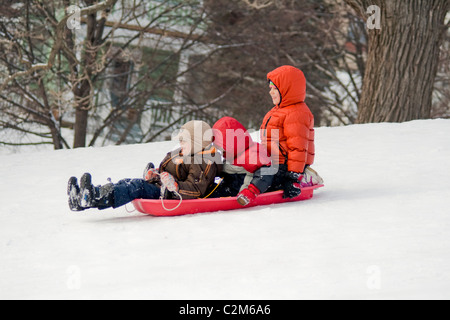 Due ragazzi di età compresa tra 5 e 6 scorrevole verso il basso con nevoso girl età 7 collina in un parco della città. St Paul Minnesota MN USA Foto Stock