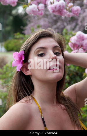 Pretty Woman in abito giallo esterno con fiori viola da un albero e guardando il visore Foto Stock
