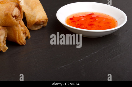 Involtini primavera con peperoncino dolce salsa di immersione sul grigio scuro dello sfondo in ardesia. Foto Stock