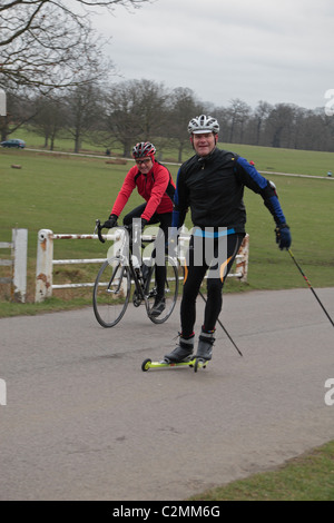 Un cross country sciatore su pattini da strada e un ciclista fuori la formazione in Richmond Park, Richmond, Surrey, Regno Unito. Foto Stock