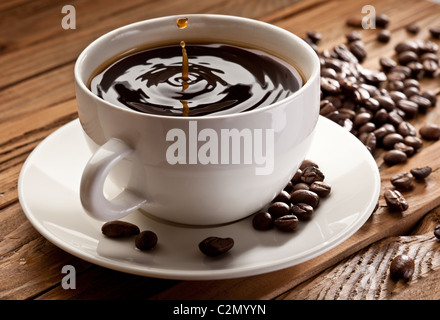 Goccia che cade in una tazza di caffè. Su uno sfondo di legno Foto Stock