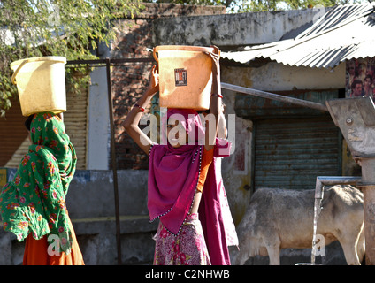 Grazioso villaggio di giovani donne che portano la benna piena di acqua fresca pulita prelevata dal pozzo nel villaggio rurale di Rajasthan in India. Foto Stock