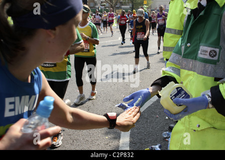 Il runner accetta vaselina dal volontario St John Ambulance sulla rotta della Maratona di Londra Foto Stock
