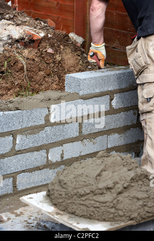 Muratore costruendo un muro con mezza brezza di cemento blocca la costruzione di un blocco di parete di ritegno nel Regno Unito Foto Stock