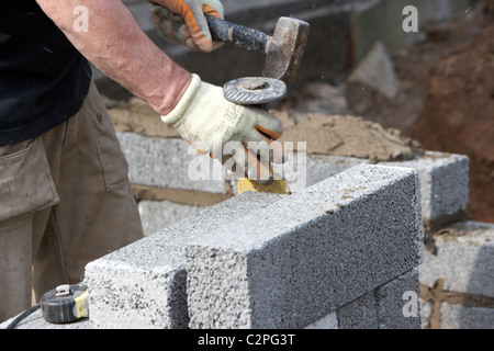 Muratore con un martello e scalpello per mattoni rafforzare per tagliare la metà brezza di cemento blocca la costruzione di un blocco di parete di ritegno nel Regno Unito edilizia Foto Stock