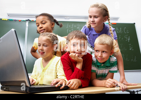 Ritratto di smart studentesse e schoolboy guardando il laptop con blackboard sullo sfondo Foto Stock