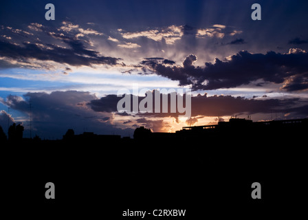 Raggi del sole al tramonto tra le nuvole prima della tempesta sulla città silhouette Foto Stock