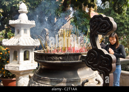 Chiudere orizzontale di una signora pregando davanti brucia incenso in un grande incensiere a Tran Quoc Pagoda (Chùa Trấn Quốc) di Hanoi Foto Stock