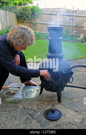 Donna che utilizza una ghisa Giardino Chimenea per cucinare e barbeque cibo barbecue nel giardino estivo del Regno Unito Foto Stock