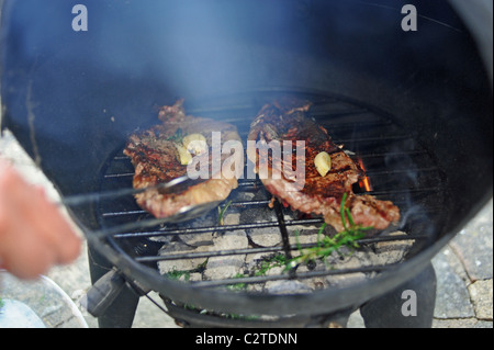 Cottura della carne di manzo bistecche su una ghisa Giardino Barbecue Chimenea barbecue nel giardino REGNO UNITO Foto Stock