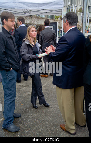 Utilizzo di un notebook, una giovane donna giornalista reporter conduce un colloquio con un nuovo proprietario di auto in San Francisco, CA. Foto Stock