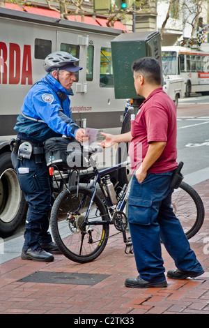 Una bicicletta montata la polizia parcheggio operaio dà una violazione biglietto per il conducente di un illegalmente parcheggiato il carrello in San Francisco, CA Foto Stock