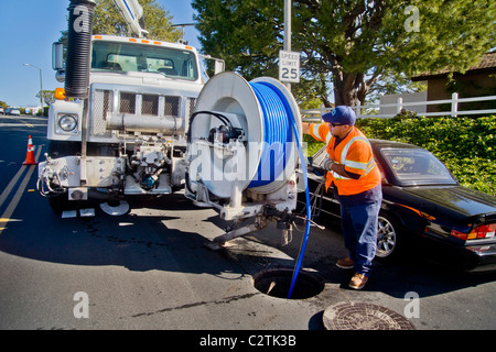 Utilizzando un carrello montato sistema di aspirazione, un tecnico pulisce un intasato di fognature in Laguna Niguel, CA. Nota giubbotto di sicurezza con fasce catarifrangenti Foto Stock