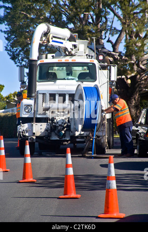 Utilizzando un carrello montato sistema di aspirazione, un tecnico pulisce un intasato di fognature in Laguna Niguel, CA. Nota giubbotto di sicurezza con fasce catarifrangenti Foto Stock