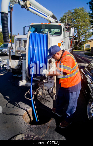 Utilizzando un carrello montato sistema di aspirazione, un tecnico pulisce un intasato di fognature in Laguna Niguel, CA. Nota giubbotto di sicurezza con fasce catarifrangenti Foto Stock