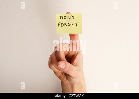 Bigliettino giallo dicendo non dimenticare su una donna di dito con off-muro bianco sullo sfondo Foto Stock