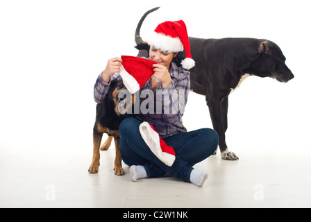 Donna felice con Santa hat seduta con le gambe incrociate sul pavimento e cercando di mettere cappelli sulle sue teste di cani per la loro preparazione Foto Stock