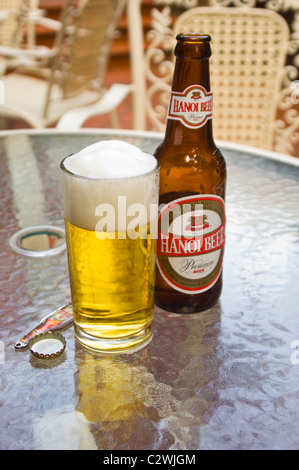 Verticale fino in prossimità di un bicchiere pieno e una bottiglia di birra di Hanoi su un tavolo. Foto Stock