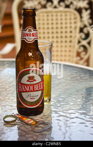 Verticale fino in prossimità di un mezzo bicchiere vuoto e una bottiglia di birra di Hanoi su un tavolo. Foto Stock