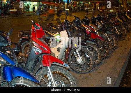 Vista orizzontale di una linea di ciclomotori e scooter parcheggiato sul marciapiede in una fila di Hanoi di notte. Foto Stock
