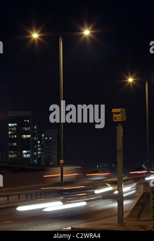 Sentieri di luce dei veicoli che passano un GATSO o fotocamera velocità di notte sul modo Aspen vicino a Canary Wharf Foto Stock