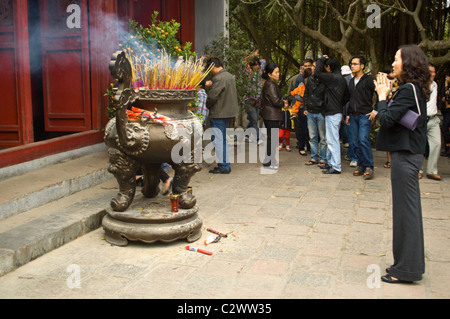 Chiudere orizzontale fino a una giovane donna orante presso un grande turibolo pieno di bruciare incenso a Ngoc Son Temple nel centro di Hanoi. Foto Stock