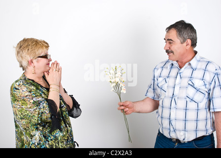 Adulto medio marito offrendo fiori a sua moglie e lei è entusiasta e piacevolmente sorpreso Foto Stock