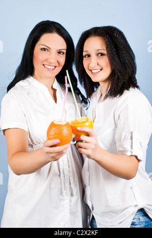 Giovani belle donne due amici sorriso in piedi insieme e tenendo succo di arancia e mandarino tagliati nelle sue mani Foto Stock