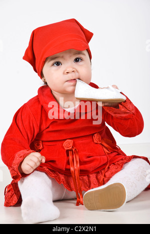 Bellissima bambina vestito in abito rosso holding e mangiare una scarpa bianco Foto Stock