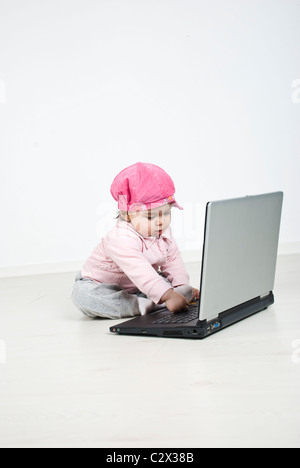 Bambina seduto in una stanza con pavimento in legno e utilizzo di computer portatile Foto Stock