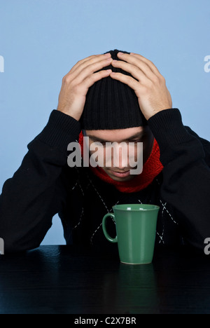 Premuto giovane uomo in nero pullover e cappuccio permanente al tavolo con le mani sulla testa e di essere preoccupato Foto Stock