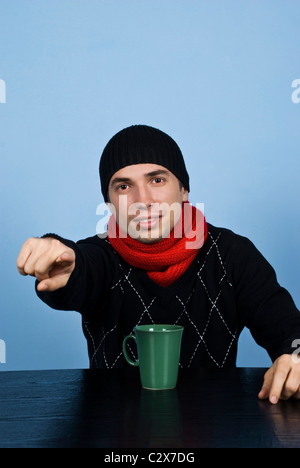 Giovane uomo vestito in abiti invernali in nero e rosso e seduta a tavola rivolto a voi Foto Stock