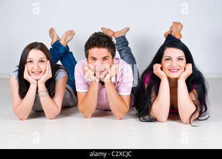 Tre amici sdraiato sul pavimento in laminato in una fila con le gambe in alto e tenendo le mani su facce Foto Stock