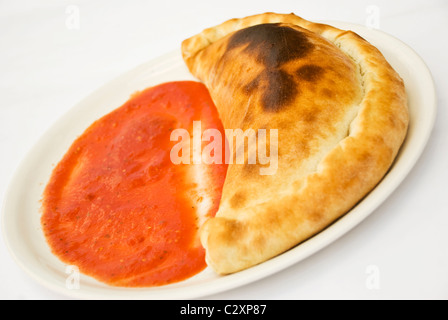 Pizza Calzone con salsa su una piastra bianca Foto Stock