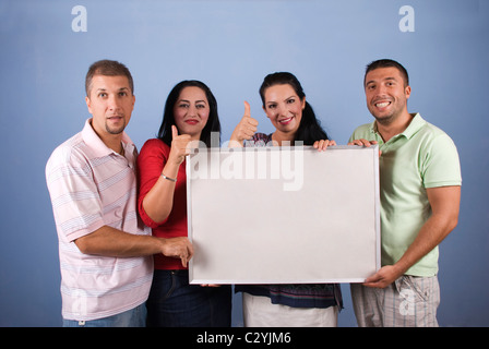 Quattro amici felice tenendo un'intestazione vuota e dando pollice in alto su sfondo blu Foto Stock