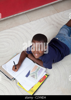 Ragazzo giovane facendo i compiti sul tappeto, Johannesburg, Sud Africa Foto Stock