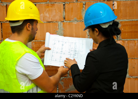 Indietro di due architetti con casco lavorando in una casa in costruzione e la holding blueprint,fuoco selettivo su piano Foto Stock