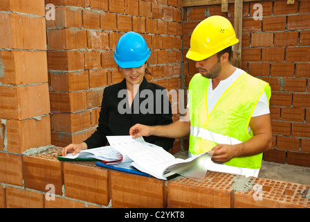 Costruzioni lavoratori cercando su blueprint e le cartelle in una casa non finita con il muro in mattoni Foto Stock