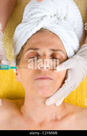 Senior donna ottenendo un iniezione di Botox alla sua guancia Foto Stock