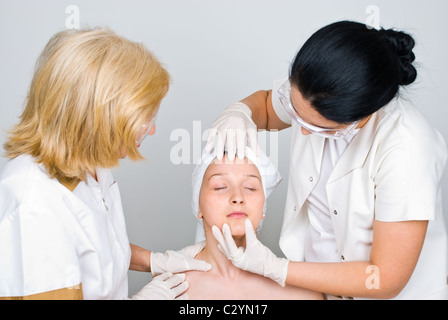 Due medici di esaminare la donna la pelle del viso e la preparazione per la sua procedura di botox Foto Stock