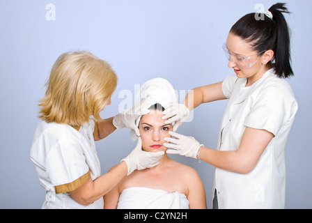 Due chirurghi plastici esaminare donne giovane donna pelle e tenendo le mani con guanti di gomma sulla faccia Foto Stock