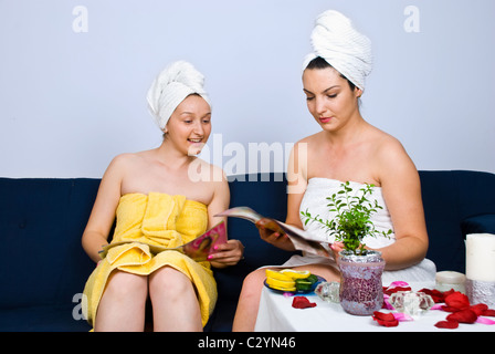 Due belle donne seduta sul lettino nella sala di attesa di spa resort e lettura di riviste Foto Stock