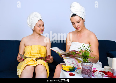 Due giovani donne seduti sul divano in una sala di attesa a spa salone lettura di riviste e di conversazione Foto Stock