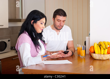 Metà adulto giovane calcolare le loro spese nella loro cucina a casa Foto Stock