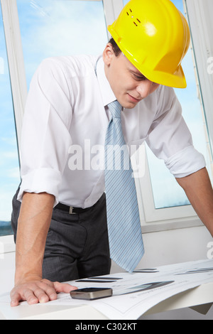 Ritratto di architetto nel casco guardando blueprint in office Foto Stock