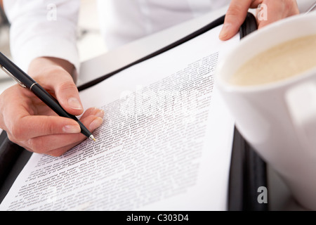 Close-up di imprenditrice la mano che tiene la penna sul documento con tazza bianca nelle vicinanze Foto Stock