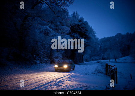 Piccola vettura si muove lentamente sulla strada ghiacciata in Cotswolds, Swinbrook, Oxfordshire, Regno Unito Foto Stock