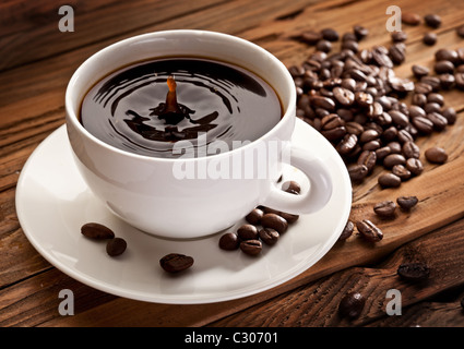 Goccia che cade in una tazza di caffè. Su uno sfondo di legno Foto Stock