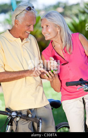 Felice senior l uomo e la donna giovane in bicicletta e insieme utilizzando un telefono intelligente al di fuori nella luce del sole Foto Stock