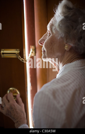 Senior donna tramite una catena di sicurezza della porta anteriore Foto Stock